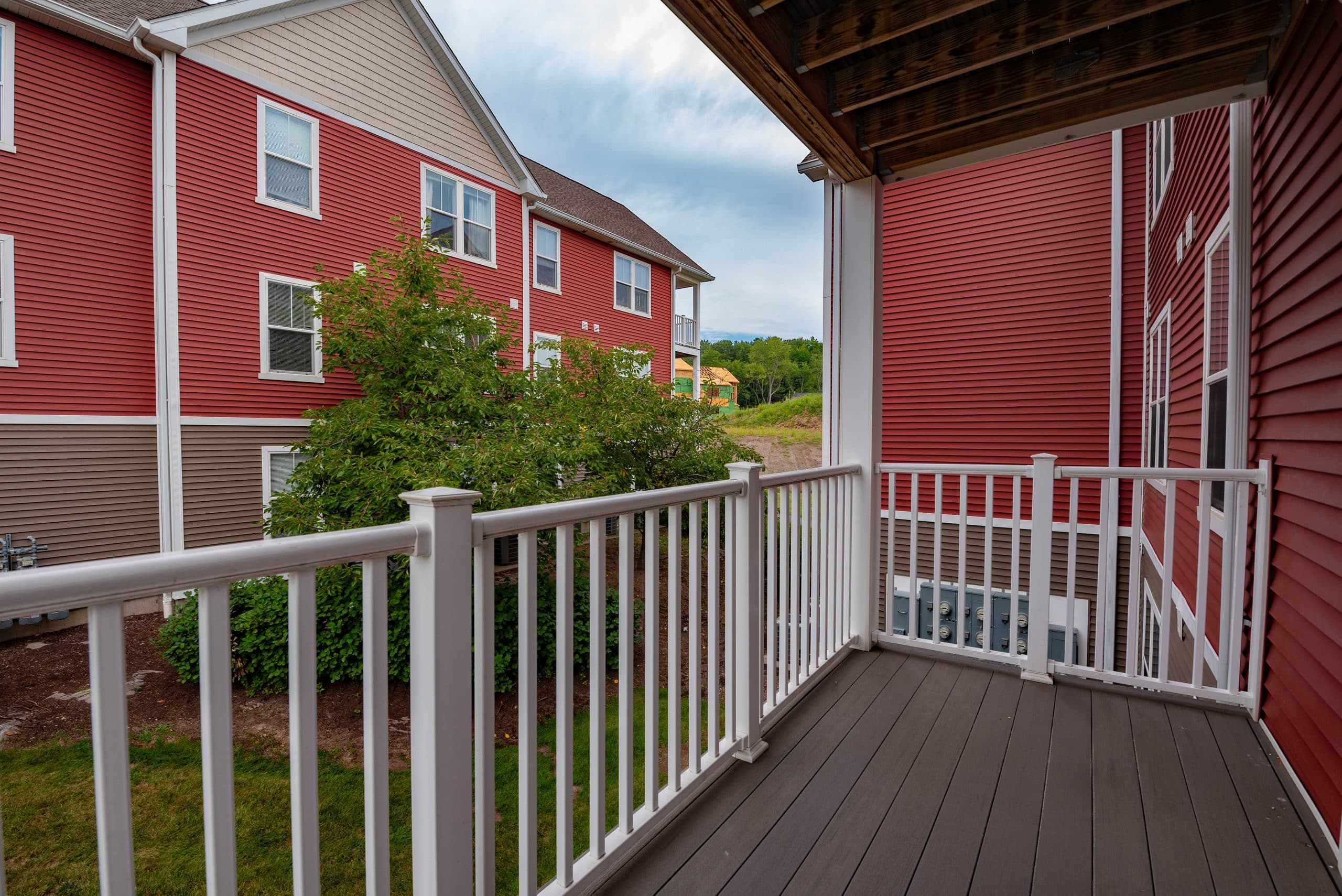 A covered private balcony with white railings looking across to the red-clapboard buildings