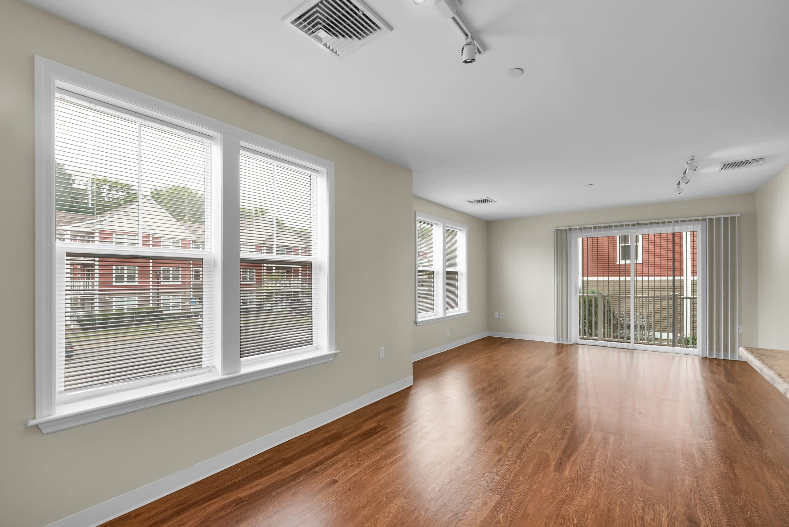 A bright living room with two wide windows and a sliding door to the balcony