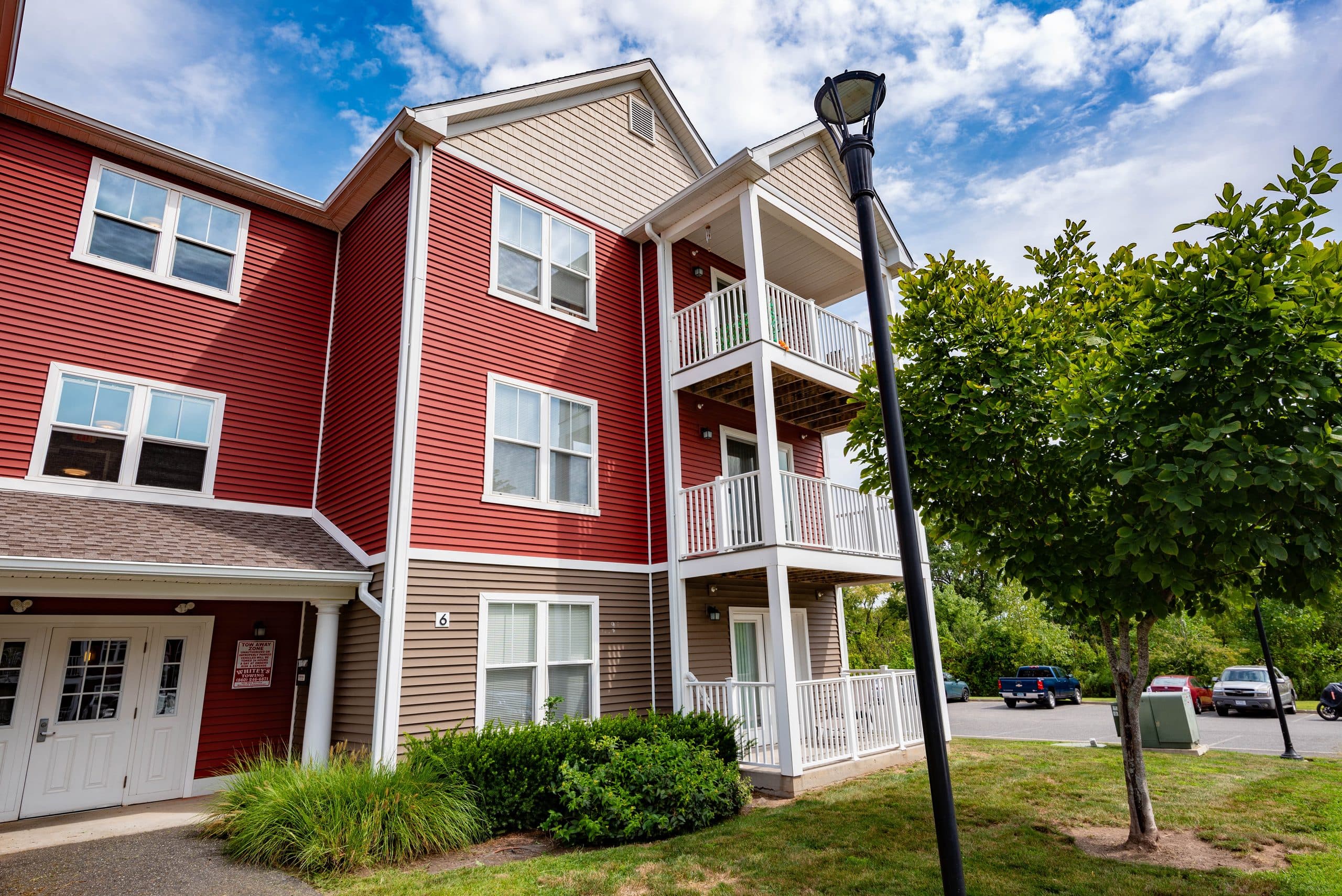 A Brook Hill Village building entry with stacked private balconies above it on a clear summer afternoon