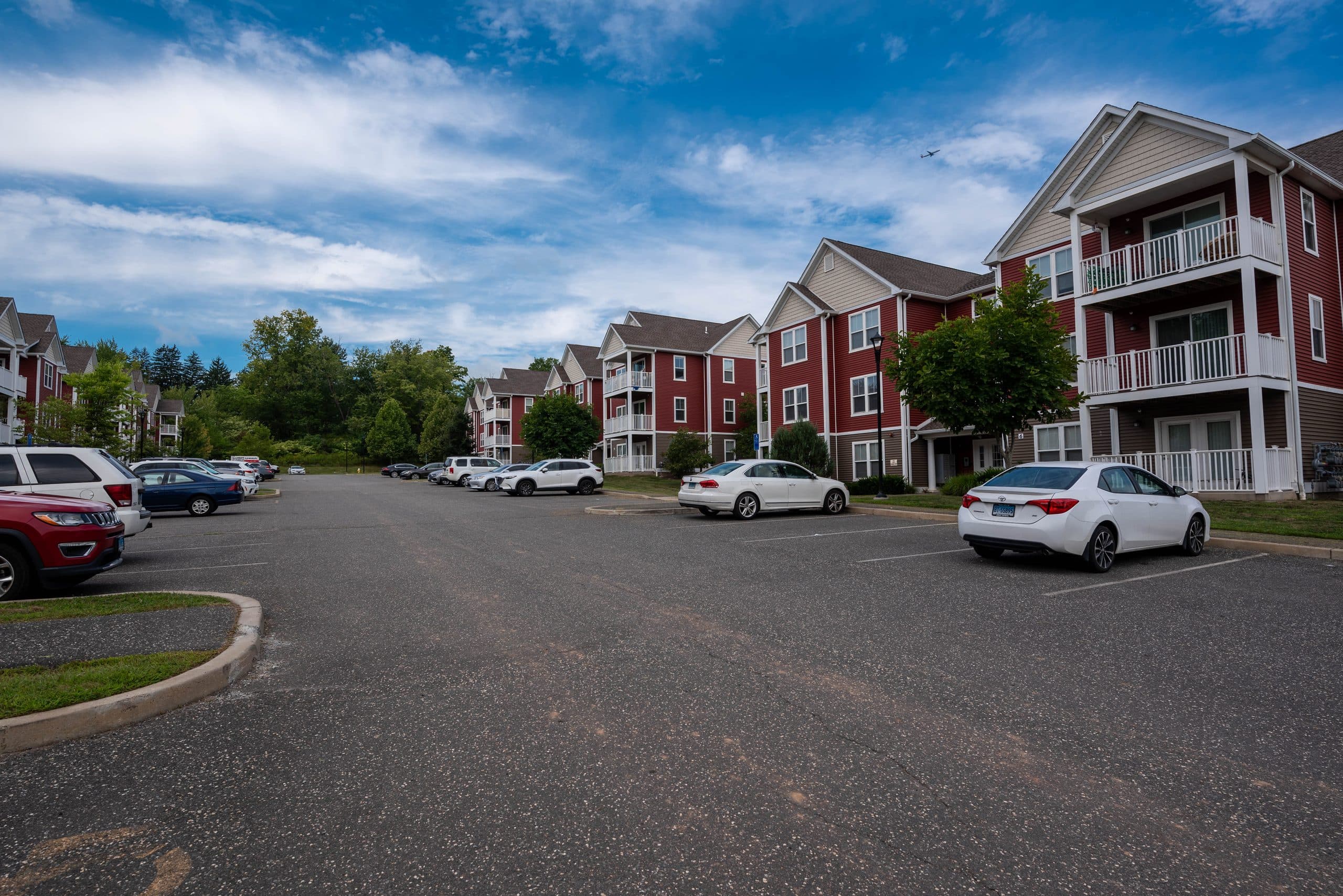 The resident drive at Brook Hill Village running past a row of red-clapboard apartment buildings under a blue summer sky
