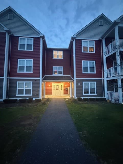 Paved walkway leading to the illuminated glass doors of a Brook Hill Village building