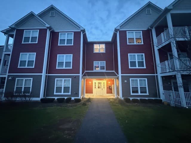 A Brook Hill Village building at dusk, its glass entry doors lit from inside