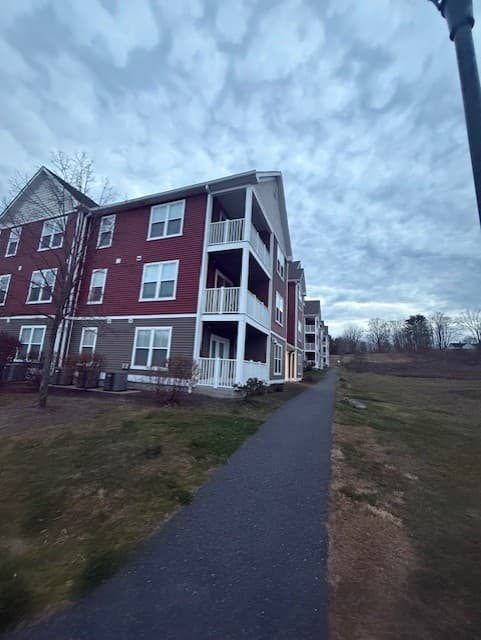 A paved walking path running alongside a Brook Hill Village building toward open field