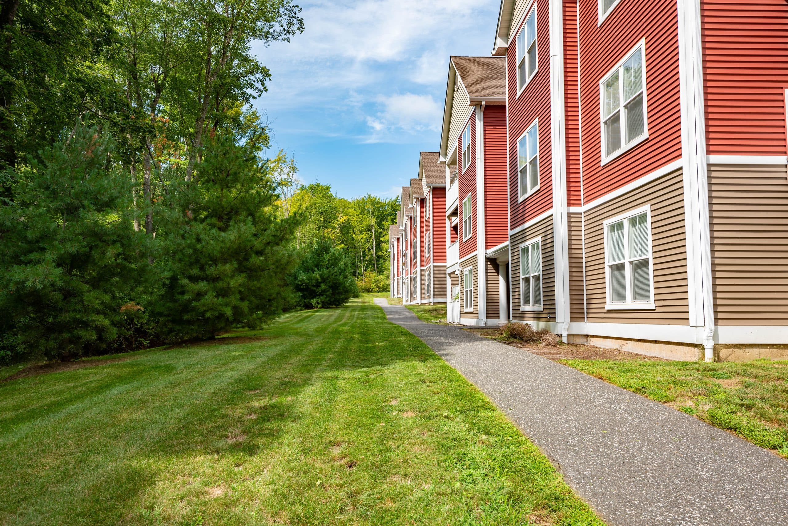A paved walking path between a long lawn and a row of red and tan apartment buildings